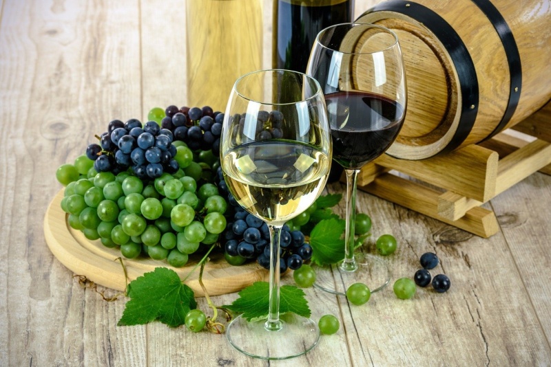 Two glasses of wine next to some bunches of white and red grapes